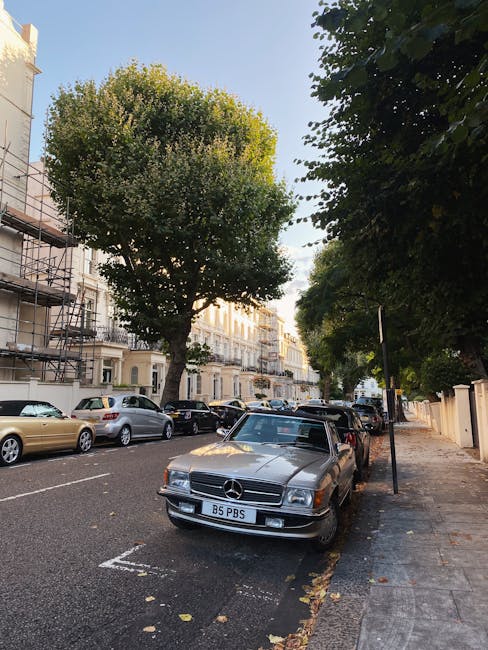 Exterior view of a brick building with six large sash windows, four on the ground floor and two on the upper floor, with white window frames and curtains. The centre features a dark blue wooden door set within a white stone surround, with a small columned portico above. The entrance area is paved with light-colored stone and bordered by a gravel surface. In front of the building, there is a narrow pathway lined with short black bollards. The scene is taken during daytime under overcast weather, with bare tree branches partially visible at the top left and right corners, suggesting a winter season. The image relates to home relocation and furniture transport, consistent with the services provided by Man with Van Bloomsbury, who may assist with loading or unloading in such premises during house moves or removals near Russell Square.