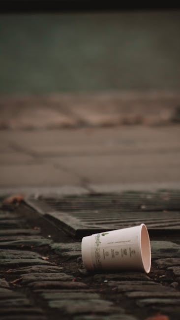 An outdoor scene showing a pile of rubbish and discarded household items, including black garbage bags, a yellow plastic container, an old, dirty armchair, and various packaging materials, all situate